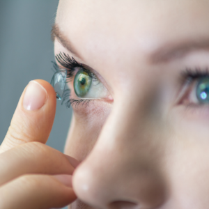 Woman putting on a contact lens on her right eye.
