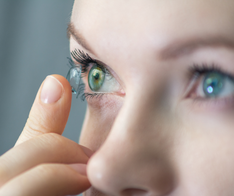 Woman putting on a contact lens on her right eye.