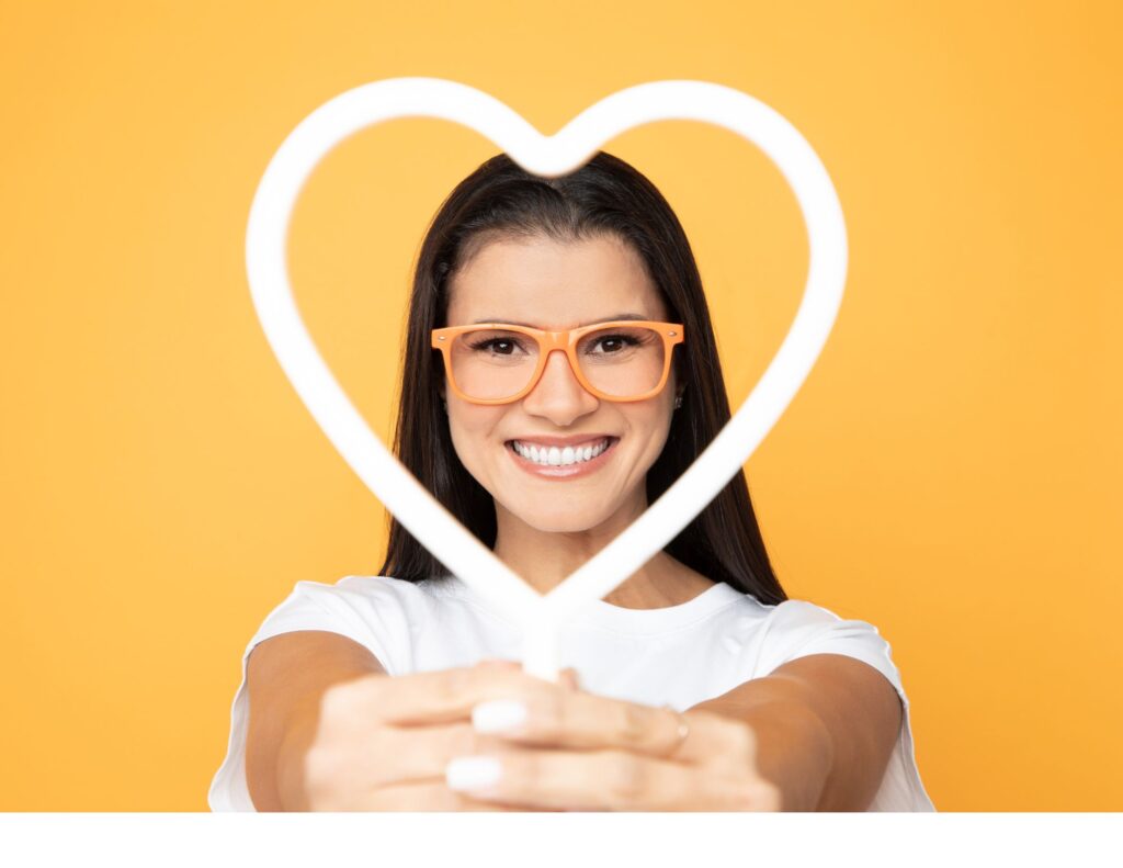 Gisele Crespo, owner of Mango Optic, wearing orange glasses and looking through a heart shaped display.