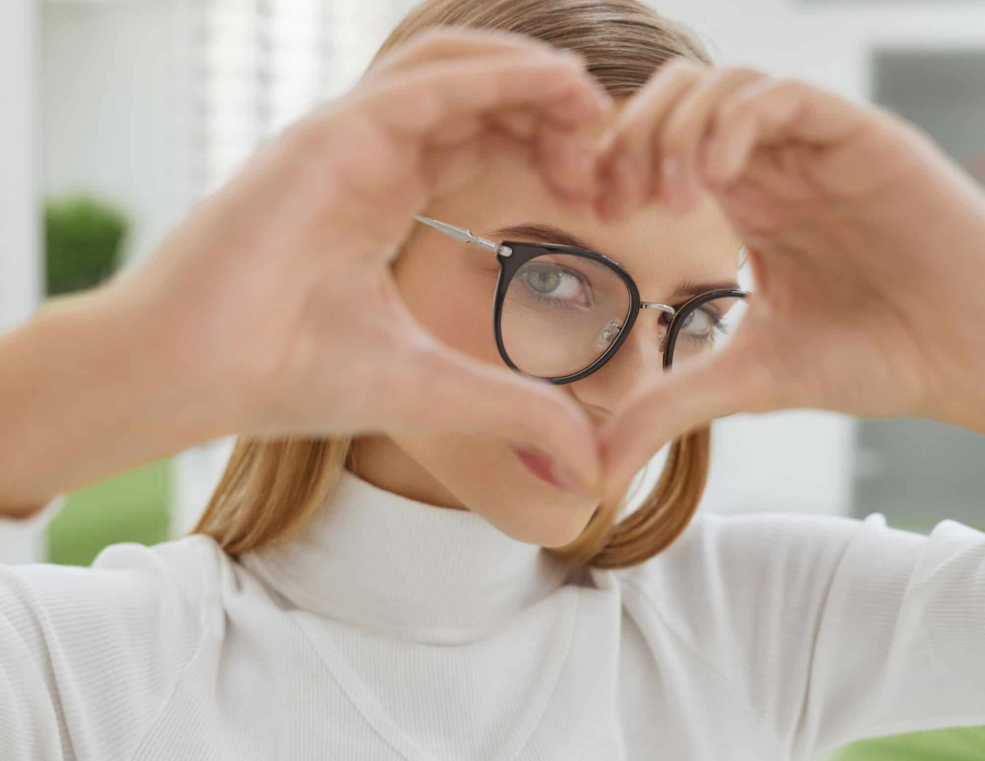 Woman wearing glasses from Mango Optic, making the heart symbol with her hands.